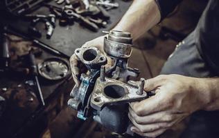 las manos de los mecánicos sostienen la turbina de un motor de automóvil foto