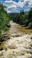 Strong flow and boiling of water in mountain river with splashes. Fast stream in the Carpathians, Ukraine. Stones in a mountain river. Natural background of water. Close-up. photo