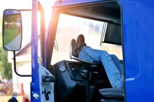 el conductor del camión descansa en la cabina del camión con los pies en el volante foto