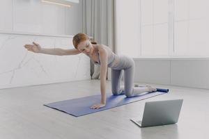 mujer joven practicando yoga por video tutorial. ejercicio de postura clases en casa en cuarentena. foto