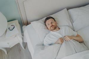 Handsome stressed young caucasian male lying in bed with his eyes open photo