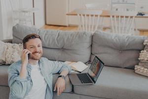 Young male office worker working from home talking on phone with his co-worker photo