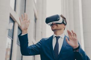 Businessman in virtual reality glasses using VR goggles while standing on city street outdoors photo