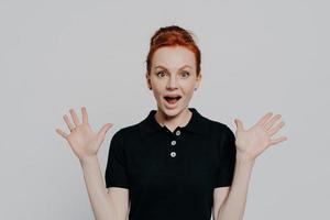 Young surprised emotional ginger girl raising hands and opening mouth with shocked face expression photo