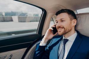 propietario de un negocio feliz sentado en el asiento trasero del coche y hablando por teléfono foto