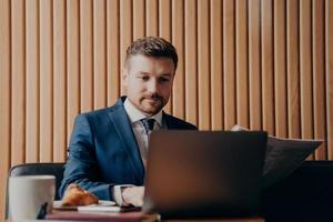 Portrait of handsome elegant financier in suit working on laptop in cafe photo