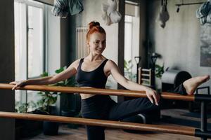 Happy young woman good stretch posing in fitness studio during barre workout photo