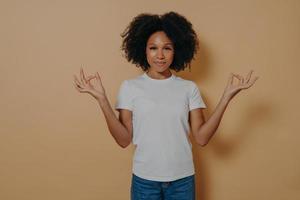 pacífica joven afroamericana manteniendo las manos en gesto de mudra, aislada en una pared beige