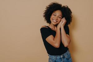 Cute woman keeping hands near face and dreaming of something good, isolated over beige wall photo