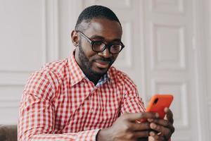 Cheerful millennial biracial man using smartphone, sitting at desk photo