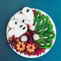 Plate of fresh kiwi, pomergranate, cherimoya, grapes and rambutan isolated over blue background. Exotic fruit. Art food concept photo