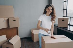 Mover is packing cargo with duct tape. Young lady is wrapping cardboard boxes with packing tape. photo