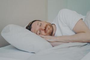 Close up view photo of bearded young male fall asleep in his bed