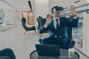 Exited CEO in VR headset enthusiastically testing app on laptop sitting in business centre lobby