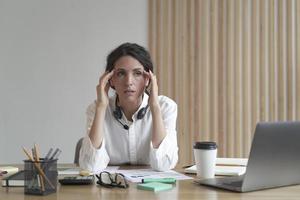 mujer de negocios frustrada que se siente cansada mientras está sentada en la oficina, que sufre de dolor de cabeza en el trabajo foto