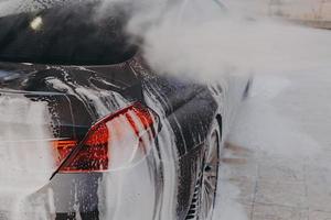 Professional car wash with high pressure washer and cleansing foam outdoors