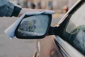 Hand of man washing car side rear view mirror with microfiber cloth rag, wiping water drops photo