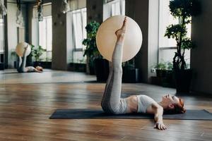 mujer joven haciendo ejercicios para las piernas con pelota de pilates mientras está acostada en la alfombra de yoga foto
