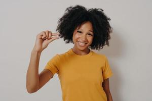 Cheerful smiling African American woman gestures small size with fingers photo