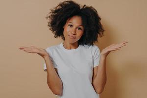 Mixed race female being unsure and having some doubts while posing against beige wall photo