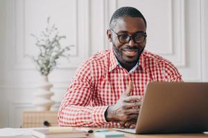 Young smiling african american businessman talking with business partner by video call on laptop photo