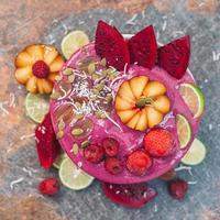 Food and art concept. Beautifully designed fruit. Ice cream with pink pitaya, slices of red dragon fruit, strawberry, raspberry, lime, coconut flakes, pumpkin seeds photo