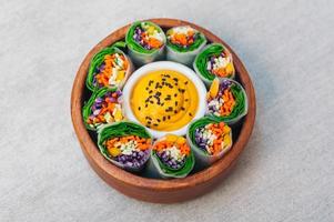 Green vegetarian spring rolls in bowl around curry sauce. Appetizing rolls filled with carrot, cucumber and purple cabbage, made of spinach. photo