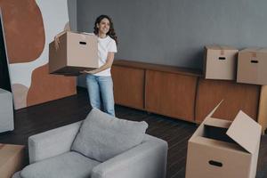 Happy young woman relocates alone and carrying a box. Single spanish lady moves. photo