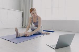 Young adult happy woman enjoying yoga practising stretching asana by online lesson. photo
