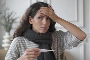 Sad sick young Italian woman wearing knitted scarf around neck suffering from flu cold at home photo