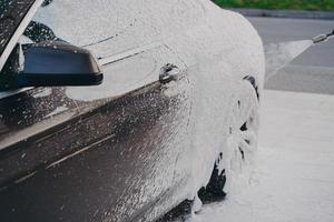 Black luxury car in white snow foam during car wash outdoors photo