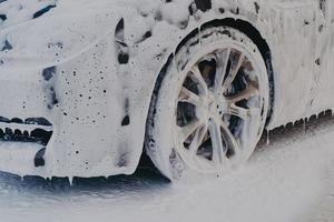 rueda de coche en espuma de jabón blanco en la estación de servicio de lavado de coches