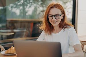 hermosa mujer profesional pelirroja freelancer trabaja en poses de computadora portátil en un café al aire libre