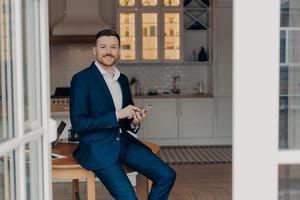 Bearded guy entrepreneur in suit using modern gadgets in his apartment photo