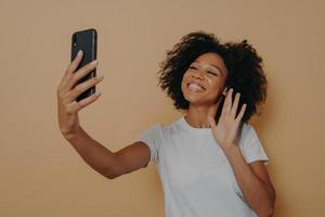Positive happy mixed race woman waving with hand at camera during video call on modern smartphone photo