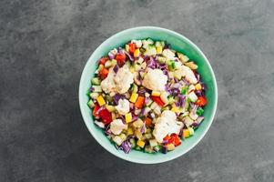 vista superior de ensalada de verduras frescas con coliflor, col morada, pimiento rojo picado y pepino. deliciosa comida en un tazón. concepto de alimentación y nutrición foto