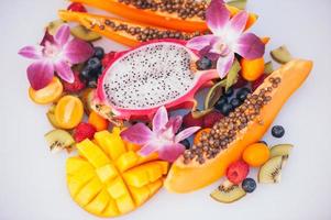 Fresh organic exotic fruits on white background. Ripe dargon fruit, papaya, kiwi, mango with kumquat, decorated with beautiful orchids. photo