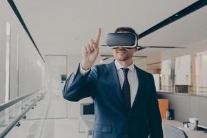 empresario masculino sonriente usando gafas vr para visualización en 3d, señalando con el dedo foto