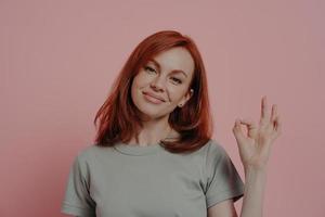 mujer sonriente dando su aprobación mientras posa aislada sobre el fondo rosa del estudio foto