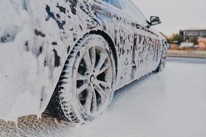 vehículo en espuma jabonosa blanca durante el lavado regular de autos al aire libre, lavado automático con jabón foto