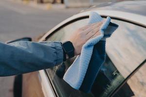 limpieza de manos masculinas en la ventana lateral del coche con trapo de microfibra