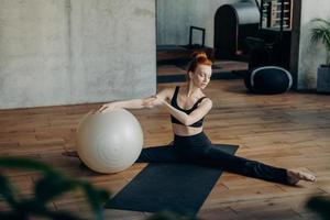 mujer joven en posición dividida haciendo ejercicio con fitball en el estudio de fitness