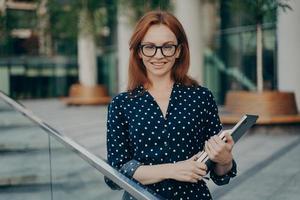 Prosperous businesswoman poses outdoor in stylish outfit carries necessary items for work photo