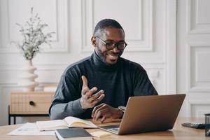 African-American young businessman in glasses having conference online with employes via video call photo