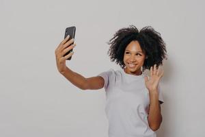 Happy young female waving at camera while having video call with best friend on modern smartphone photo