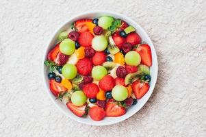 Healthy fresh fruit salad in bowl. Slices of strawberry, raspberry, kiwi, tangerines, blueberry on plate. Delicious fruits. Vegeterian dish. Ripe berries. photo