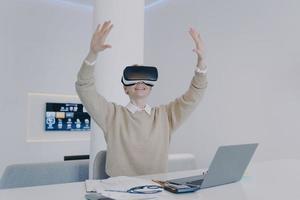 Young happy european woman in VR glasses is raising hands. Concept of corporate innovation.