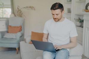 Serious young man using laptop computer for remote work from home photo