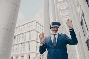 Futuristic image of happy businessman using virtual reality 3d goggles while standing outdoors photo