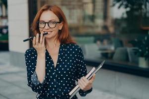 Red haired successful businesswoman records voice message keeps smartphone near mouth photo